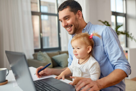 Father working on laptop with daughter in his lap