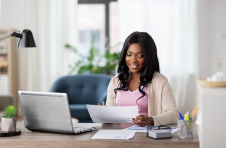 Happy woman with laptop and papers at home office