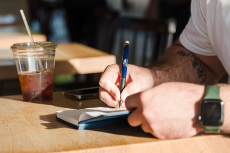 student writing with a UTSA pen at a coffee shop