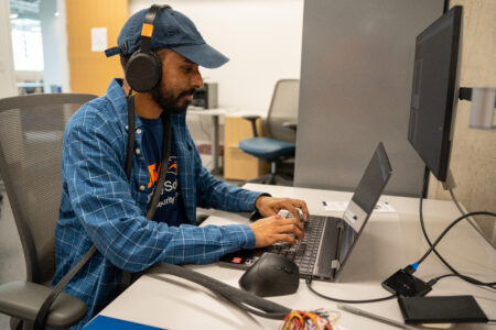 Man with hat and headphones wearing jean jacket sitting at computer