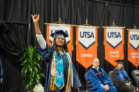 Woman holds up UTSA's sign as she crosses the stage at commencement