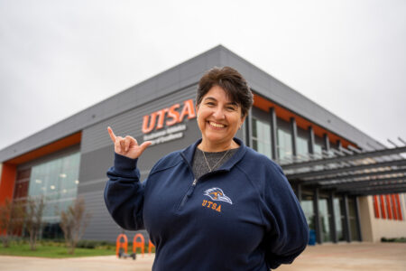 Brenda Davila holding up the "Roadrunner" sign in front of the UTSA RACE building