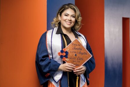 Elsa Trejo in gown holding a cap that says "For my family and my angels in Heaven that watch over me