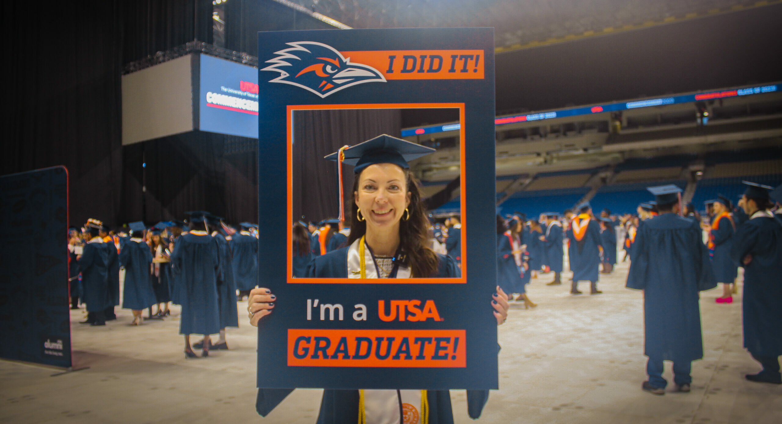 Online Communication Degree graduate at commencement holding a photo frame that says "I did it! I am a UTSA Graduate!"