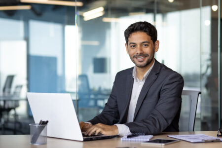 Young businessman, man smiling and looking at camera while sitting inside office.