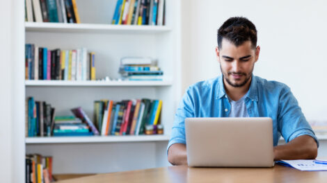 Man working with computer at desk in front of bookshelf