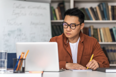 middle-aged man taking an online class on his laptop and taking notes on his notebook