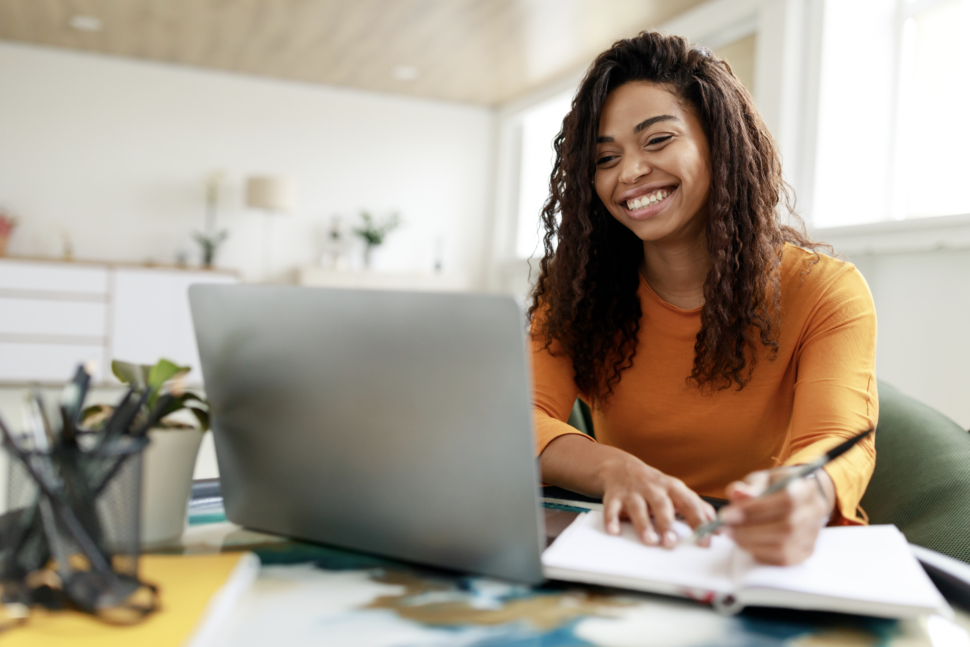 Distance Education. Portrait of smiling woman sitting at desk, using laptop and writing in notebook, taking notes, watching tutorial, lecture or webinar, studying online at home looking at screen