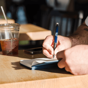 student writing with a UTSA pen at a coffee shop