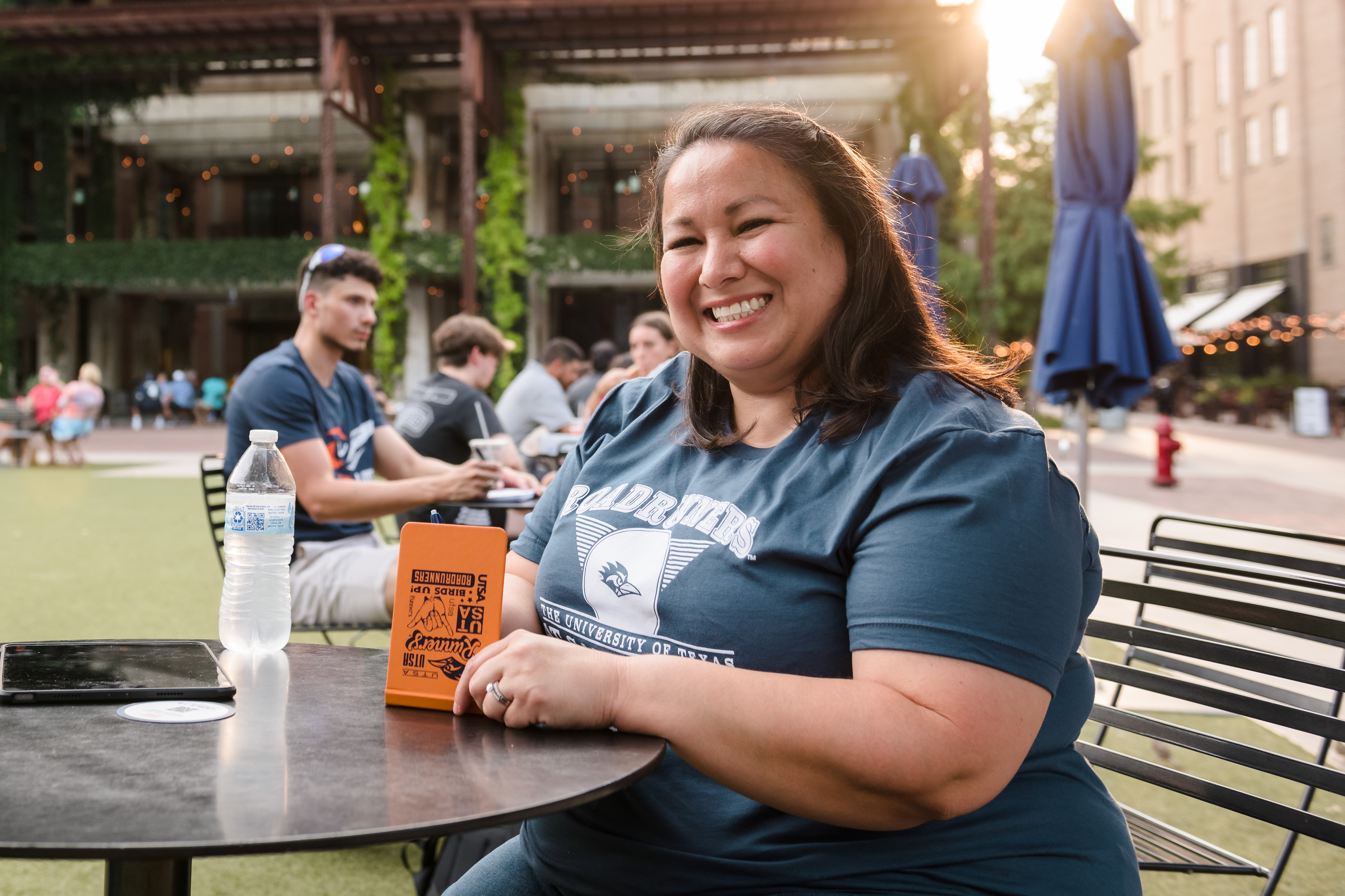 Felicia Carrola - UTSA Online graduate sitting at an outdoor table with a UTSA notepad