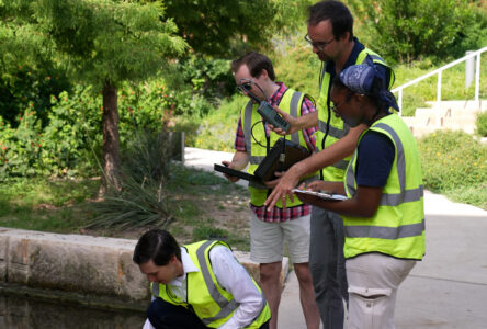 Four people in bright yellow vests holding clipboards and studying the water for a project.