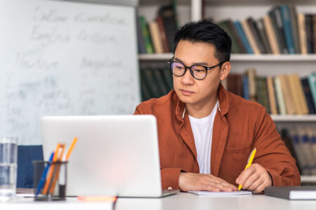 Man looking at computer and writing in notebook