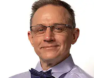 Man with glasses, a purple dress shirt and a bow tie.