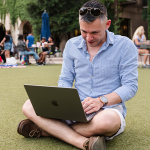 male student sitting with his laptop in a lawn